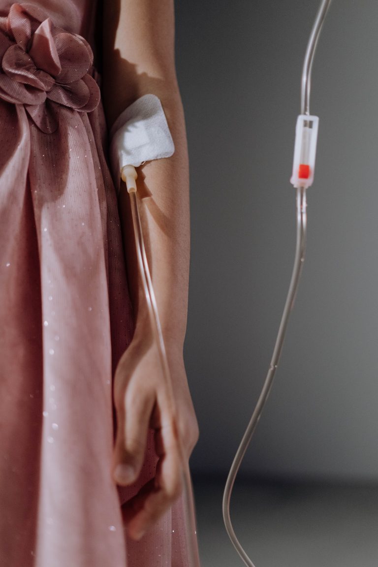 צילום תקריב של ילדה או אישה בשמלה ורודה המחוברת לצינורית עירוי רפואי (אינפוזיה) בבית חולים